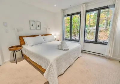 a bedroom with a bed with white sheets and windows at Scandi Lakefront Condo Near Big Boulder Ski! in Lake Harmony