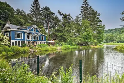 a blue house with a pond in front of it at Lakefront Poconos Retreat with Hot Tub, Near Hiking! in Bear Creek Village