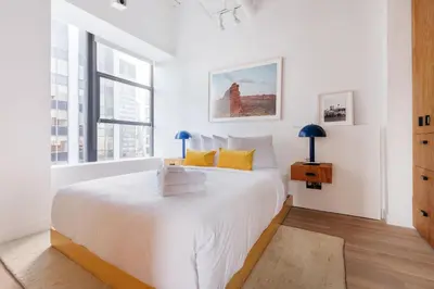 a white bedroom with a large bed and a window at Placemakr Wall Street in New York