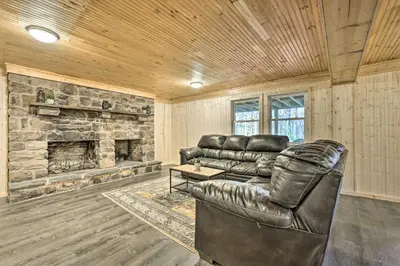 a living room with a leather couch and a stone fireplace at Game Room, Fire Pit and Deck Spacious Poconos Home! in Lake Harmony