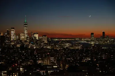 a city skyline at night with the moon in the sky at The Ritz-Carlton New York, NoMad in New York