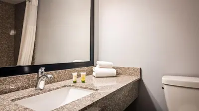 a bathroom with a sink and a toilet and a mirror at Travelodge by Wyndham Bellmawr in Bellmawr