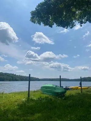 a green boat sitting on the grass next to a lake at The Nook Lodge - cabin with hot tub at Shawnee and Camelback Mtn in East Stroudsburg