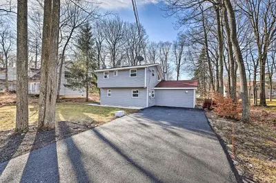 a white house with a garage in the woods at Hot Tub, Fire Pit and Game Room Tobyhanna Home! in Tobyhanna