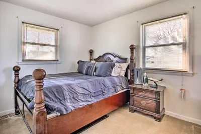 a bedroom with a bed and a nightstand and two windows at House with Pellet Smoker and Grill, 1 Mi to Lake! in Bellmawr
