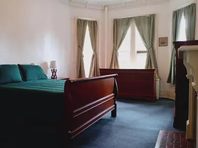 a bedroom with a bed and a dresser and two windows at Mini Mansion Hotel near public transportation is the yellow and green house on the corner of 8th st and Madison avenue in Plainfield