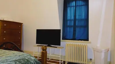 a bedroom with a computer monitor on a table next to a window at Mini Mansion Hotel near public transportation is the yellow and green house on the corner of 8th st and Madison avenue in Plainfield