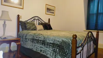a bedroom with a bed and a table with a lamp at Mini Mansion Hotel near public transportation is the yellow and green house on the corner of 8th st and Madison avenue in Plainfield