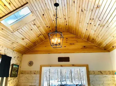 a chandelier hanging from a wooden ceiling with a window at Charming 120-year-old farmhouse by the creek. in Starlight