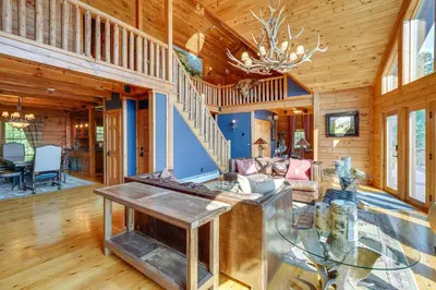 a living room with a staircase and a chandelier at Luxury Log Cabin with EV Charger and Mtn Views! in Blairstown