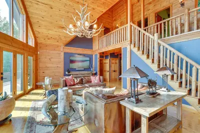 a log home living room with a staircase and a chandelier at Luxury Log Cabin with EV Charger and Mtn Views! in Blairstown