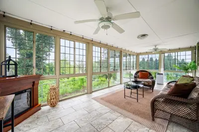 a living room with a ceiling fan and large windows at Downingtown Manor - 1900s Farmhouse with Creek Views in Downingtown