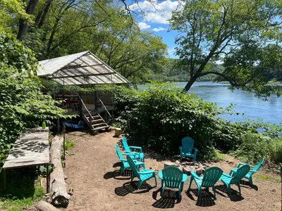 a group of chairs sitting in the sand near the water at Slumberland at the River's Edge in Pond Eddy