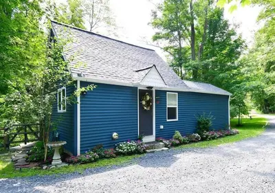 a blue tiny house with flowers in front of it at Cottage at Millpond Falls - A Romantic Escape in Warwick