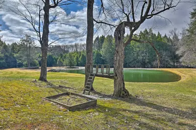 a bench sitting between two trees next to a lake at Catskill Getaway on 6 Acres with Swimming Pond! in Liberty