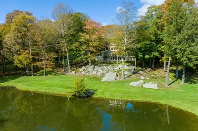 a house on a hill next to a pond at Catskill Getaway on 6 Acres with Swimming Pond! in Liberty