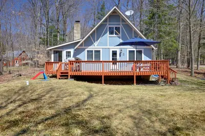 a house with a large deck with an umbrella at Walk to Beach Pocono Lake Cabin with Pool Access! in Pocono Lake