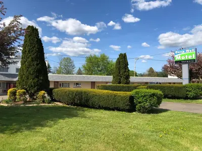a sign for a motel with bushes and a lawn at DEEPWELL MOTEL in Owego