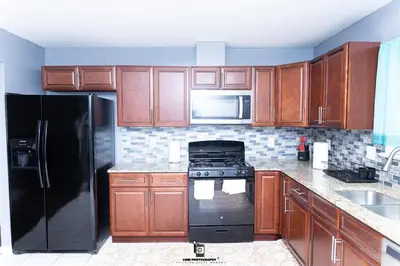 a kitchen with wooden cabinets and a black refrigerator at Beautifully Designed & Spacious Apartment in Newark 10mins from EWR Airport, Close to NYC and Beth Israel Hospital in Newark
