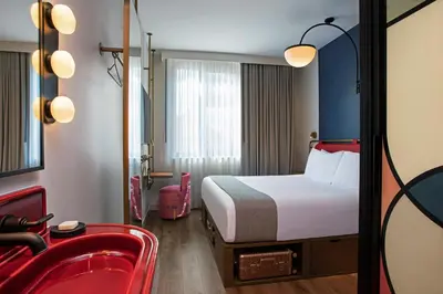 a hotel room with a bed and a red chair at Moxy NYC Lower East Side in New York