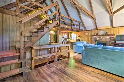 a living room with a staircase and a blue couch at Game Room and Fire Pit Tree-Lined Pocono Lake Cabin in Pocono Lake