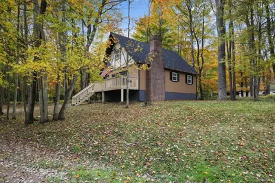 a small house with a deck in the woods at Game Room and Fire Pit Tree-Lined Pocono Lake Cabin in Pocono Lake