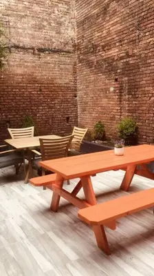 two picnic tables and chairs in a room with a brick wall at 1850s historic Row House 7min train to NYC with private backyard in Jersey City