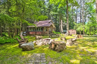 a log cabin in the middle of a yard with rocks at Secluded and Quiet Pocono Mountain Cabin with Hot Tub! in Kunkletown