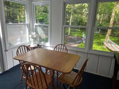 a table and chairs in a room with windows at Romantic Pocono house - stream, lake, beach, pool, firepit in Locust Lakes Village