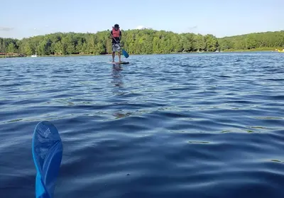 a man standing on a paddle board in the water at Peaceful Pocono Lakefront, beach, pools, firepit, pets in Arrowhead Lake
