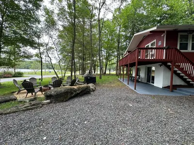 a house with chairs and a log in front of it at Peaceful Pocono Lakefront, beach, pools, firepit, pets in Arrowhead Lake
