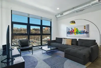 a living room with a couch and a large window at Dharma Home Suites Hoboken in Hoboken
