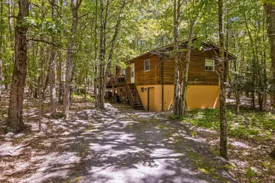 a log cabin in the woods with a path leading to it at The Cozy Cabin in Albrightsville