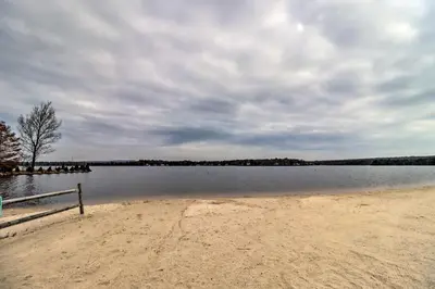 a beach with a bench in the middle of a lake at Walk to Wolf Run Lake Cottage with Furnished Deck in Albrightsville