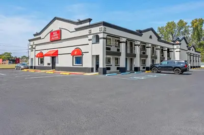 a building with a car parked in a parking lot at Red Carpet Inn and Suites in Bellmawr