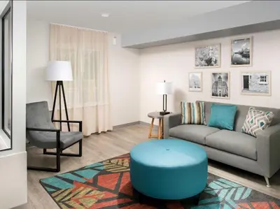 a living room with a couch and a blue stool at WoodSpring Suites Harrisburg Linglestown in Harrisburg