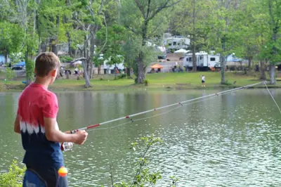 a young boy standing in a lake holding a fishing rod at Lakewood Park Campground - Luxury Cabin in Barnesville