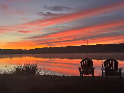 two chairs sitting in front of a lake at sunset at The Cabin in Pocono Summit