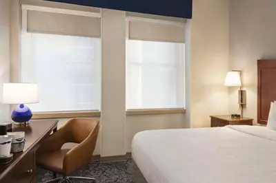 a hotel room with a bed and a desk and two windows at Hampton Inn Manhattan/Downtown- Financial District in New York