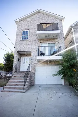 a brick house with a white garage door and stairs at Urban Oasis Spacious 3BR 2BA Patio Near NYC EWR American Dream Mall in Newark