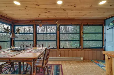 a dining room with a table and chairs and windows at Deck and Forest Views Secluded Cresco Cabin! in Cresco