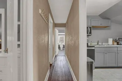 a hallway leading to a kitchen with white cabinets at Suites on Seneca - Gorgeous One Bedroom Apartment in Harrisburg