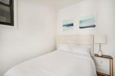 a white bed in a bedroom with two pictures on the wall at 69-2B Prime Lower East East BRAND NEW 1br Apt in New York