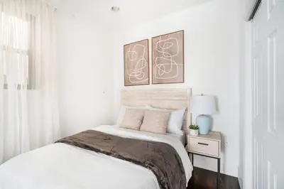 a white bedroom with a bed and a table with a lamp at 69-5B I Stylish Lower East Side 1BR Apt BRAND NEW in New York