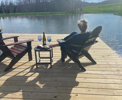 a woman sitting in a chair on a dock with wine glasses at FRENCH WOODS FARMHOUSE Catskills Upper Delaware River Hancock NY in Hancock