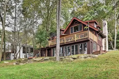a large house with a large deck in the woods at Lakefront Cabin Pvt Beach and Dock - Sunset Marina in Arrowhead Lake