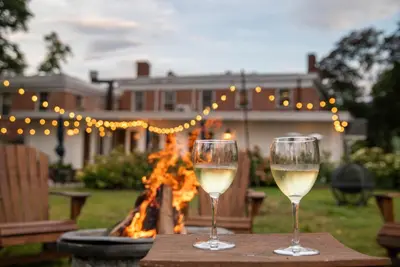 two glasses of white wine sitting on a table in front of a fire at Cromwell Manor Inn in Cornwall-on-Hudson
