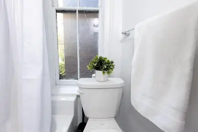 a white bathroom with a toilet and a window at E10-1 Designer East Village Townhouse 1BR in New York