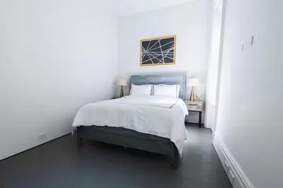 a white bedroom with a large bed with white sheets at E10-2 Designer East Village Townhouse 1BR W D in New York