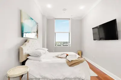 a white bedroom with a bed and a flat screen tv at XL Studio - Studio with Pool & Scenic Rooftop in Philadelphia